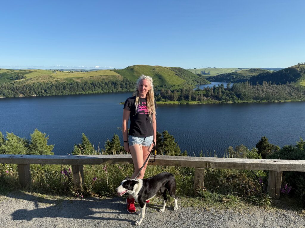female dog and female dog owner in black tshirt and shorts with a lake in the background